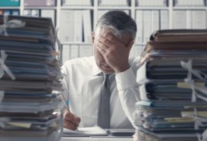 stressed-business-executive-and-piles-of-paperwork-PX89VUH-1024×699